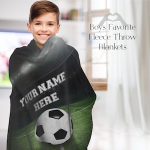 May include: A black fleece throw blanket featuring a football pitch and a football design. The blanket has the text "Your Name Here" printed on it.