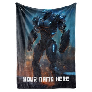 May include: A plush blanket featuring a futuristic robot design in shades of black and blue, with glowing accents. The words "YOUR NAME HERE" are printed in white at the bottom, set against a cityscape backdrop.