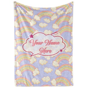 May include: A soft, purple fleece blanket with a repeating pattern of colorful rainbows and white clouds. The blanket features a speech bubble with the text "Your Name Here" in pink.