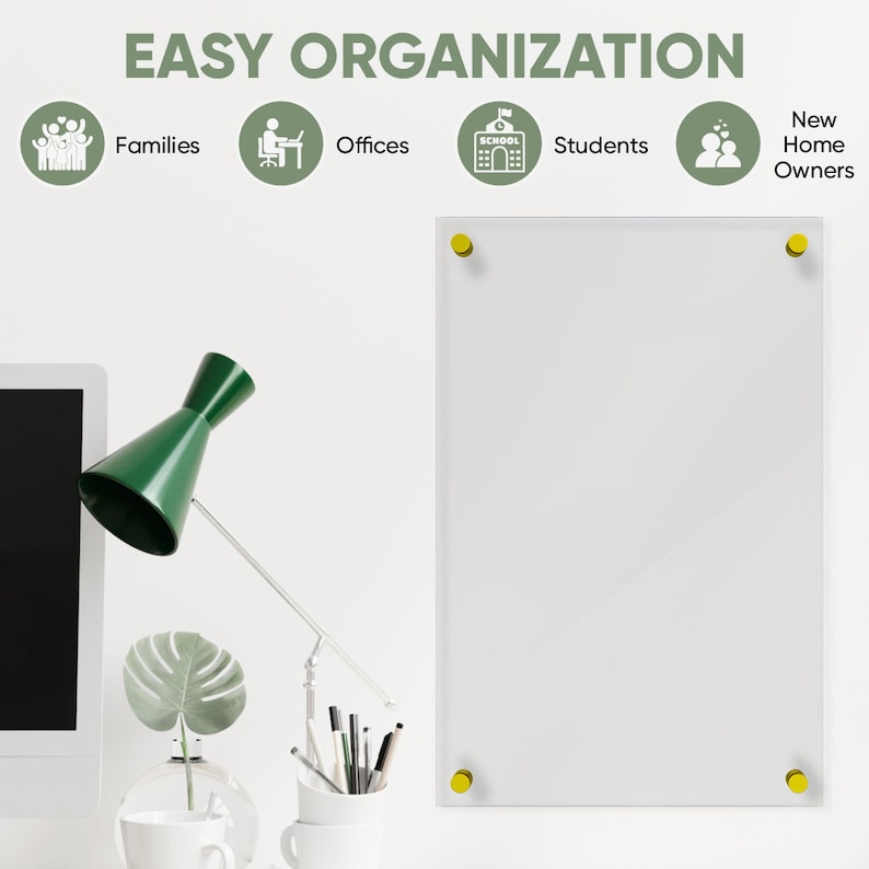 May include: A white dry erase board with gold push pins in each corner. The board is mounted on a white wall. The board is surrounded by a desk with a green lamp, a potted plant, and a computer monitor.