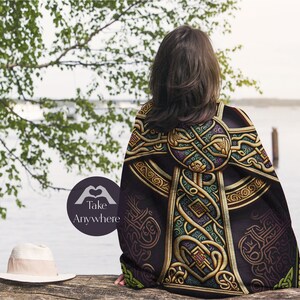 May include: A black throw blanket with a gold Celtic knot design. The blanket is draped over a person's shoulders, and the person is standing in front of a body of water.