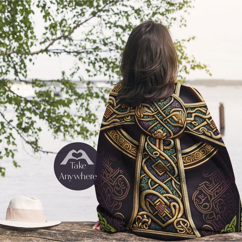 May include: A black throw blanket with a gold Celtic knot design. The blanket is draped over a person's shoulders, and the person is standing in front of a body of water.