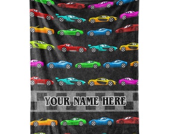Puede incluir: Una manta negra con un patrón de coches de carreras coloridos en varios colores, incluyendo rojo, verde, azul, amarillo y rosa. La manta tiene un diseño de bandera a cuadros con el texto "YOUR NAME HERE".