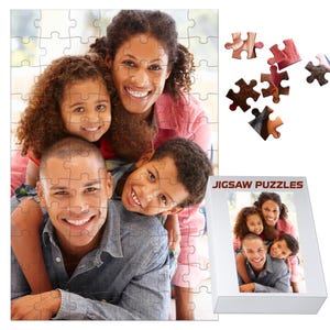 May include: A completed jigsaw puzzle featuring a family portrait, with a father, mother, and two children smiling. The puzzle is mostly assembled, with a few pieces separate. A box with the words "JIGSAW PUZZLES" is also visible.