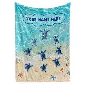 May include: A blue and white fleece blanket with a beach scene and sea turtles. The text "YOUR NAME HERE" is in a white cloud shape at the top of the blanket.