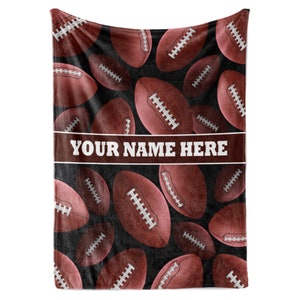 May include: A brown and black fleece blanket with a pattern of red footballs. The blanket has a white banner with the text "YOUR NAME HERE".