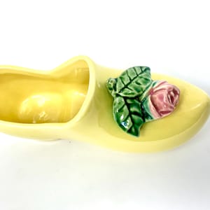 May include: A yellow ceramic planter shaped like a clog with a pink rose and green leaves.