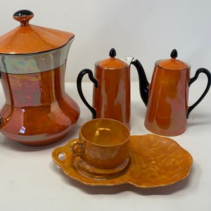 May include: A vintage orange and black tea set with a teapot, creamer, sugar bowl, cup, and saucer. The set has a glossy finish and a unique iridescent glaze.
