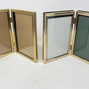 May include: Two gold-toned tri-fold picture frames. The frames are empty and have a shiny finish.