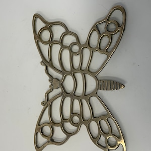 Può includere: Un sottopentola in metallo dorato a forma di farfalla con un design decorativo tagliato.