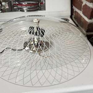 May include: A white glass ceiling light fixture with a geometric pattern. The light fixture is hanging from the ceiling and has a white cord.