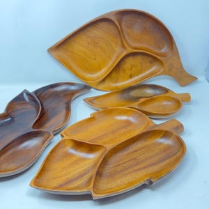 Pode incluir: Quatro bandejas de servir de madeira em forma de folhas. As bandejas são de madeira castanho escura e têm vários compartimentos.
