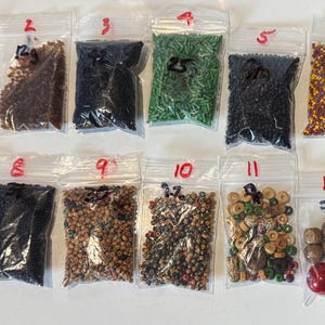 May include: Twelve small plastic bags each containing a different type of seed bead. The bags are labelled with numbers 1 through 12.