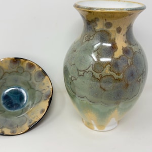 Peut inclure: Un ensemble vase et bol en céramique. Le vase est de forme bulbeuse avec un col étroit, présentant un glaçage aux teintes vertes, bleues et beiges. Le bol a une palette de couleurs similaire et un bord festonné. L'ensemble est pour la décoration intérieure.