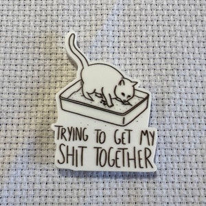 May include: White sticker with a black line drawing of a cat using a litter tray. The text below the image reads "Trying to get my shit together."