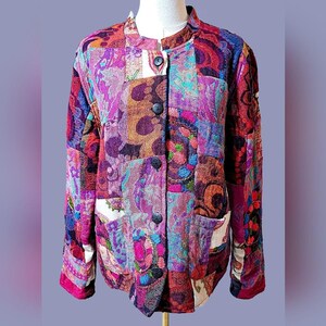 May include: A patchwork jacket with a mandarin collar and long sleeves. The jacket features a vibrant mix of paisley and floral patterns in shades of purple, pink, orange, and blue. It has black buttons and two front pockets.