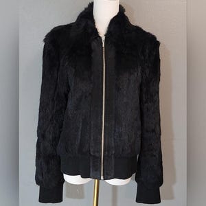 Könnte beinhalten: Schwarze Kunstfell-Bomberjacke mit Reißverschluss, gerippten Bündchen und Saum. Die Jacke wird auf einer Schaufensterpuppe präsentiert. Die Jacke hat einen hohen Kragen und lange Ärmel.
