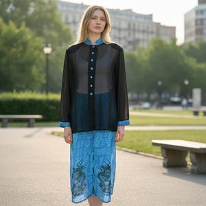 May include: A sheer black long-sleeve blouse with a mandarin collar and a vertical row of bright turquoise buttons. The blouse is paired with loose-fitting blue trousers featuring a repeating pattern and two large green dragon illustrations.