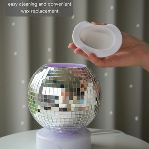 K&ouml;nnte beinhalten: Ein silberner Discokugel-Wachsschmelzer mit einem abnehmbaren wei&szlig;en Silikontablett. Der Schmelzer hat einen wei&szlig;en Sockel mit einem violetten Licht. Der Text "SCANDINORDICA&reg;" ist auf dem Sockel sichtbar.