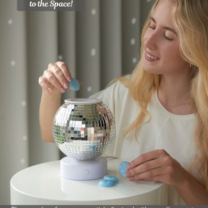 K&ouml;nnte beinhalten: Ein silberner Discokugel-Wachsschmelzer mit wei&szlig;em Sockel. Der Schmelzer steht auf einem wei&szlig;en Tisch und eine Person f&uuml;gt dem Schmelzer ein blaues Wachsst&uuml;ck hinzu. Der Text "Adds a Fun Vibe to the Space!" befindet sich oben im Bild. Geben Sie einen Wachskubus oder &auml;therisches &Ouml;l, vermischt mit etwas Wasser, in die Heizschale. Stecken Sie den Stecker in die Steckdose und schalten Sie den Schalter ein, um Ihren Raum mit einem angenehmen Duft zu f&uuml;llen.