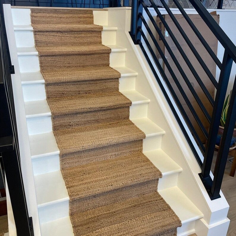 May include: A set of stairs with white risers and brown sisal carpet runner. The stairs have a black metal railing.
