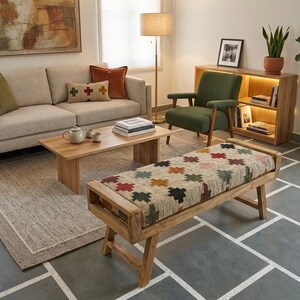 May include: A living room with a beige sofa, wooden furniture, and a patterned bench. The room includes a green armchair, a wooden bookshelf, and a rug. The scene is complemented by decorative pillows and a floor lamp, creating a comfortable space.