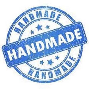 May include: A blue and white distressed circle stamp with the word "HANDMADE" in bold white letters. The word "HANDMADE" is repeated around the outer edge of the circle.