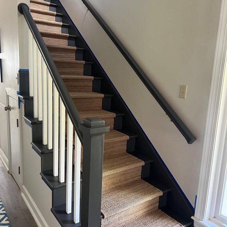 May include: A set of stairs with a black handrail and white spindles. The stairs are carpeted with a natural fiber rug.