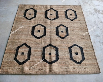May include: A rectangular jute rug with a geometric pattern. The rug is a natural tan color with a repeating pattern of black, stylized, hexagon shapes. The rug is suitable for indoor use.
