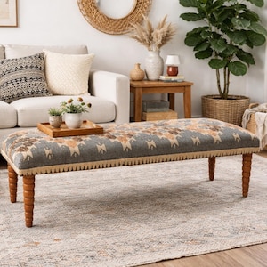 Puede incluir: Escena de salón con un banco estampado con patas de madera, un sofá color crema con cojines decorativos y una alfombra de tonos neutros. Una cesta de mimbre y plantas en macetas se suman al ambiente acogedor. El banco mide unos 152 cm de largo.