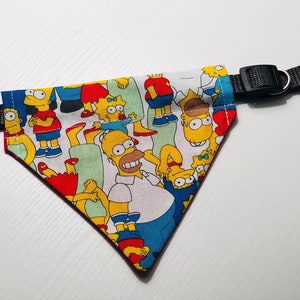 May include: A yellow, blue, and red dog bandana with a print of the Simpsons characters. The bandana has a black adjustable collar strap with a buckle.
