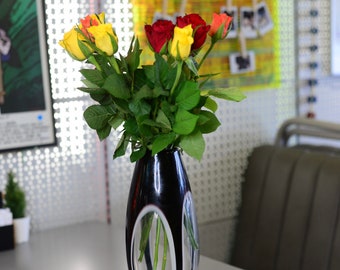 May include: A bouquet of yellow and red roses in a black and white glass vase. The vase has a unique design with oval cutouts.
