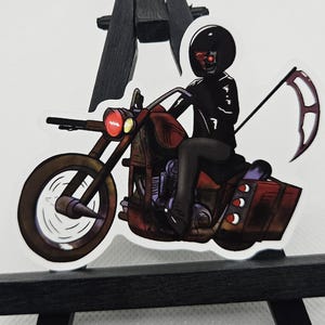 May include: A sticker featuring a cartoon Grim Reaper riding a brown motorcycle. The Reaper wears a black helmet and jacket, with red eyes. The motorcycle has a scythe attached and red headlights. The sticker is on a white background.