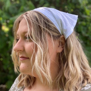 May include: A white cotton headband with a dotted pattern. The headband is tied around the head and the ends are tucked in.