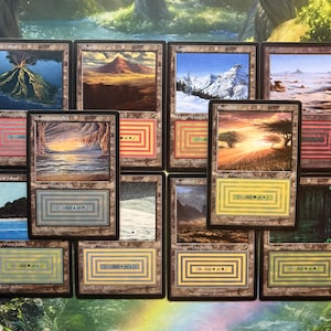 May include: A collection of Magic: The Gathering trading cards with landscape illustrations. The cards depict volcanoes, mountains, and forests, with text and geometric borders. The cards are arranged on a green and white background.