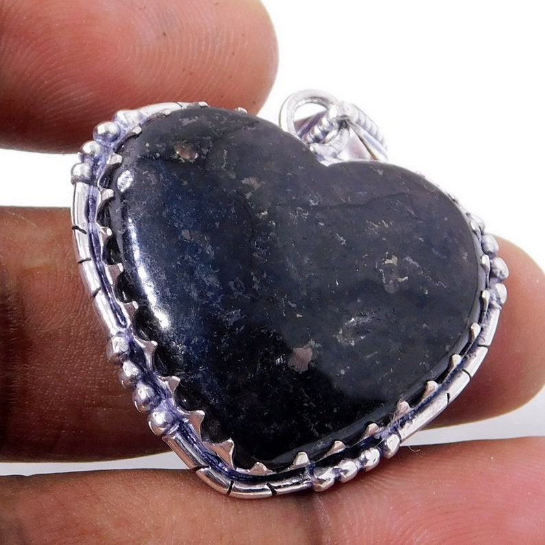 Pu&ograve; includere: Un ciondolo a forma di cuore in argento con una pietra preziosa nera. Il ciondolo ha un bordo argentato dettagliato con piccole perle.