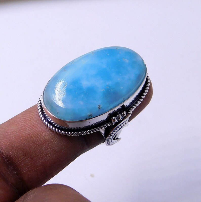 May include: A silver ring with a large oval blue gemstone. The ring has a decorative band with a crescent moon design.