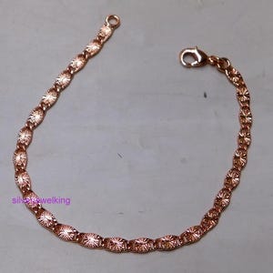 Pode incluir: Uma pulseira em tom de ouro rosa composta por uma série de elos ovais interligados, cada um apresentando um padrão texturizado semelhante a um raio de sol. A pulseira inclui um fecho lagosta numa extremidade e um pequeno anel circular.