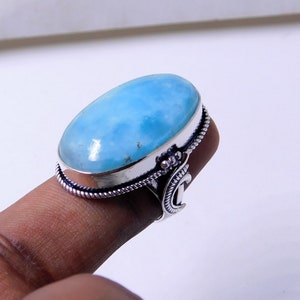 May include: A silver ring with a large oval blue gemstone. The ring has a decorative band with a crescent moon design.