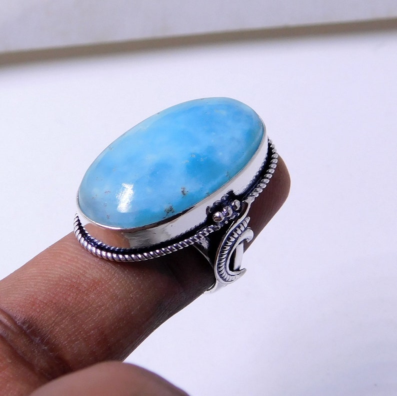 May include: A silver ring with a large oval blue gemstone. The ring has a decorative band with a crescent moon design.