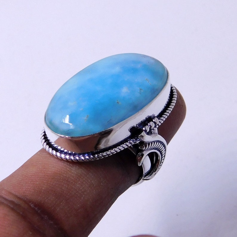 May include: A silver ring with a large oval blue gemstone. The ring has a detailed design with a rope-like band and a curved accent.