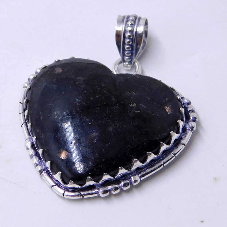 Pu&ograve; includere: Un ciondolo a forma di cuore in argento con una pietra preziosa nera incastonata in una cornice d'argento. Il ciondolo ha una balla d'argento dettagliata con piccole perle.
