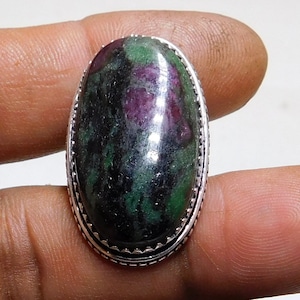 May include: Oval-shaped green and pink gemstone ring with a silver setting. The ring has a detailed border around the stone.