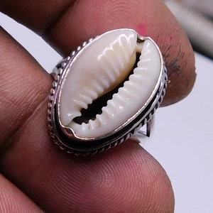 Op de afbeelding: Een zilveren ring met een witte kauri schelp in het midden. De schelp is omgeven door een zilveren band met een parelrand.