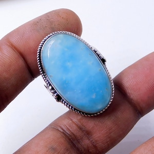 May include: A silver ring with a large oval blue gemstone. The ring has a detailed silver band with a rope-like design.
