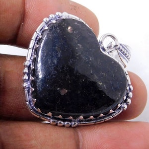 Pu&ograve; includere: Un ciondolo a forma di cuore con una pietra preziosa nera incastonata in una cornice d'argento. Il ciondolo ha un bordo dettagliato con piccole perle.