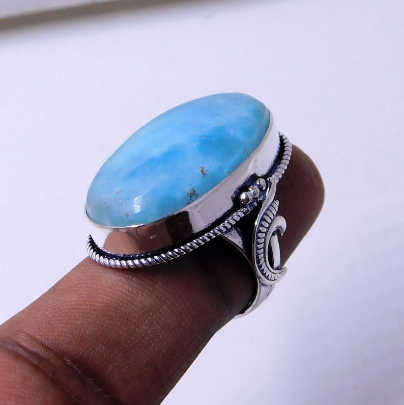 May include: A silver ring with a large oval blue gemstone. The ring has a decorative band and a crescent moon design on the side.