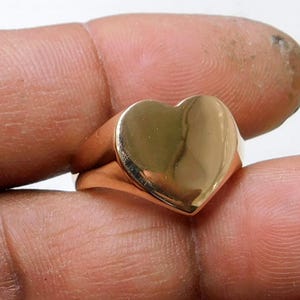 May include: A gold heart-shaped ring with a smooth, polished finish. The ring is worn on a finger.