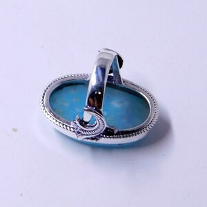 May include: A silver ring with a large oval turquoise stone set in a silver bezel. The ring has a decorative band with a crescent moon design.