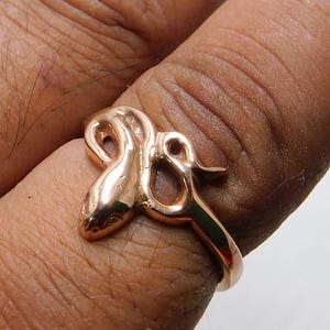 Op de afbeelding: Een roségouden ring in de vorm van een slang. De kop van de slang is gedetailleerd met kleine ogen en een gebogen lichaam dat de vinger omsluit. Een uniek sieraad.